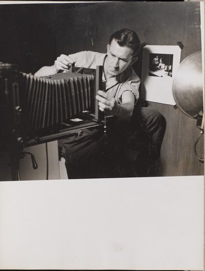 [Uomo regola il soffietto di una macchina fotografica di grande formato] da Arnold Eagle