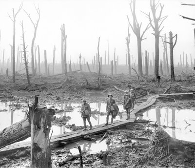 Cinque australiani, membri di una brigata di artiglieria da campo, che passano lungo una passerella su fango e acqua tra tronchi d