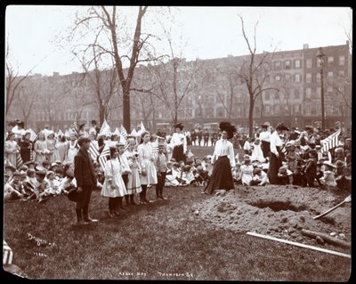 Adulti e bambini con bandiere intorno a una buca appena scavata per la piantagione di un albero nel Tompkins Square Park, New York da Byron Company