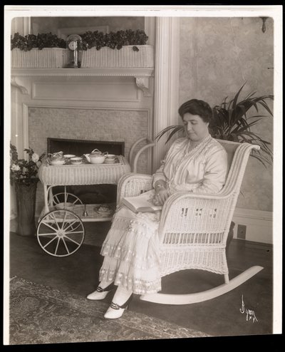 La signora Howard seduta con un libro su una sedia a dondolo nella sua casa al 200, 5th Avenue, New York, 1915-6 da Byron Company