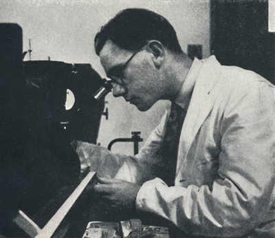 Ricercatore con microscopio che testa la struttura di una lega di alluminio da Cecil Beaton