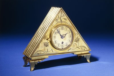 Orologio da tavolo triangolare in ottone con decorazione floreale incisa da Dagobert (attr. to) Peche
