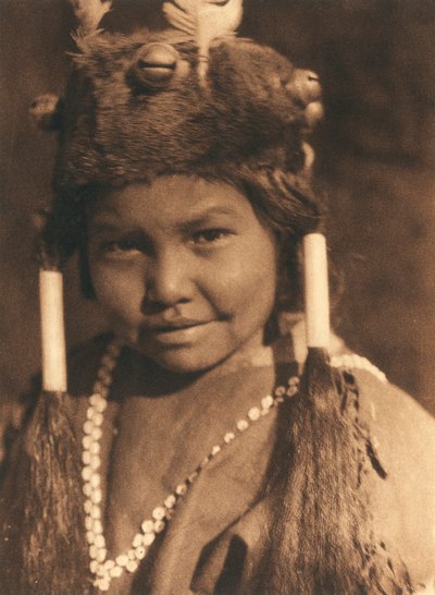 Primo piano di un ragazzo indiano americano della tribù o villaggio Klamath. Indossa un cappello di pelliccia con ghiande e piume applicate e porta i capelli in due code di cavallo da Edward Sheriff Curtis