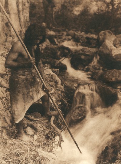 Giovane indiano americano della tribù Hupa che pesca salmoni usando un lungo bastone. Indossa una pelle di animale legata intorno ai fianchi. Dietro di lui boschi e un ruscello da Edward Sheriff Curtis