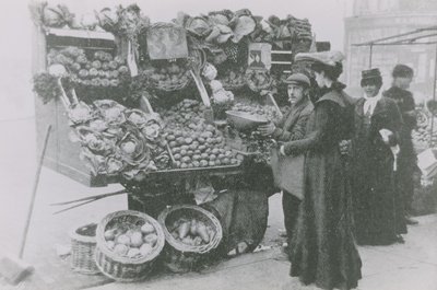 Un droghiere accanto alla sua bancarella mentre serve una donna da English Photographer