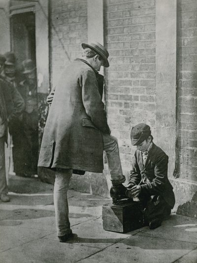 Un giovane lustrascarpe che lucida le scarpe di un uomo per strada da English Photographer