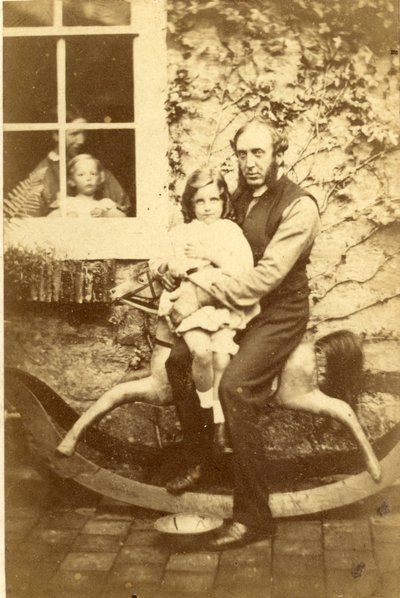 Padre e figlia seduti su un cavallo a dondolo con fratello e madre che guardano dalla finestra, 1860s da English Photographer