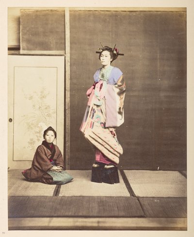 [?Geisha,] Ritratto in studio a figura intera di una giovane donna con scarpe elevate, il suo giovane assistente inginocchiato sul pavimento accanto a lei da English Photographer