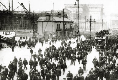 Fine del turno al cantiere navale Harland und Wolff, Belfast, Irlanda con il Titanic in costruzione sullo sfondo, 1910-11 da English Photographer