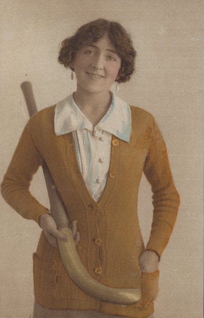 Ragazza carina, con maglione lavorato a maglia, con orecchini di perle, che tiene una mazza da hockey (foto) da English Photographer