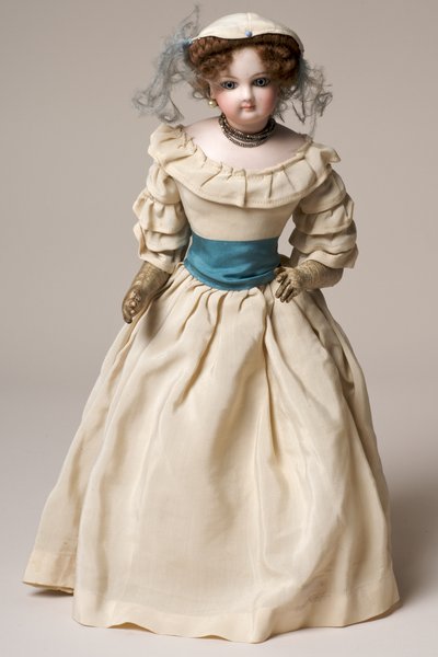 Bambola di moda in biscuit con testa girevole, vestita con un lungo abito crema e cappello (ceramica e tessuto) da English School