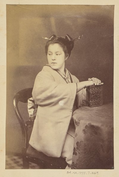 [Donna giapponese seduta con in mano un album di cartes-de-visite a un tavolo]. da Felice Beato