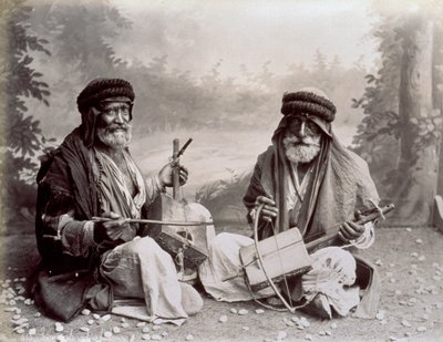 Ritratto di due musicisti arabi in abiti etnici umili. Gli uomini anziani posano in studio, seduti a terra. Dietro di loro c