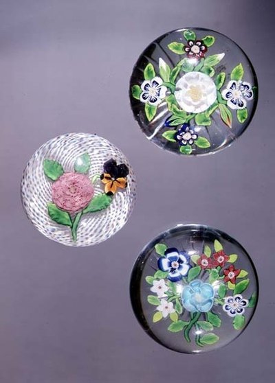 Tre fermacarte, da sinistra a destra: rosa e viola di Clichy con fondo bianco opaco a reticello, e due bouquet di Baccarat con basi a stella da French School