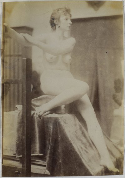 Studio di un modello femminile nudo, seduto su un podio accanto a un cavalletto e visto di fronte, nell
