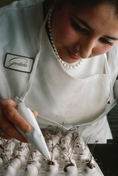 Uno chef Godiva attacca steli di cioccolato a ciliegie ricoperte di fondente. Bruxelles, Belgio da James L Stanfield