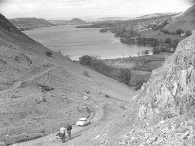 Veduta di una collina con strada, auto e persone, lago sullo sfondo da Joseph Hardman