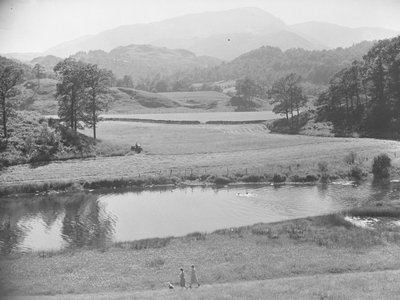 Donne che spingono un bambino nel passeggino sulla riva del fiume attraverso un prato con persone che nuotano nel fiume e un contadino che lavora al trattore nei campi e sullo sfondo le montagne. da Joseph Hardman