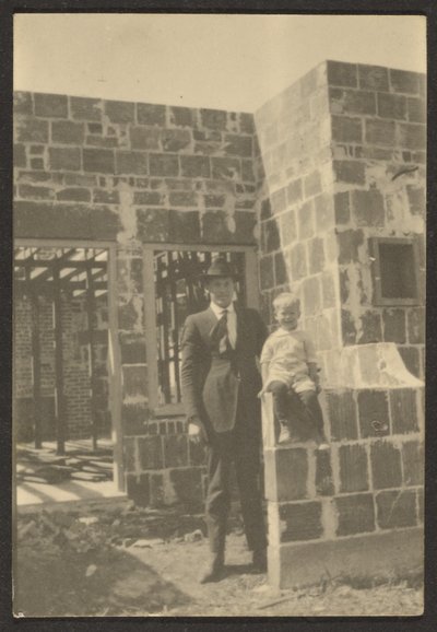 [Uomo con bambino in piedi in una casa in costruzione]. da Louis Fleckenstein