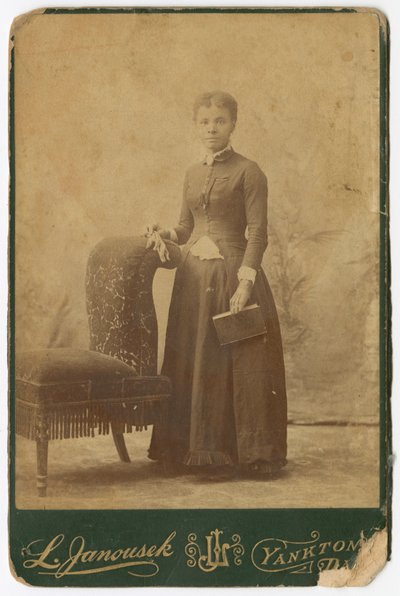 Fotografia di una donna in piedi accanto a una sedia e che tiene un libro, fine XIX secolo da Louis Janousek