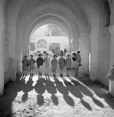 Bambini europei in uniforme scolastica sotto un arco con ombre da Maynard Owen Williams