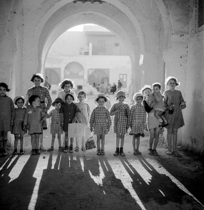 Bambini europei in uniforme scolastica sotto un arco con ombre da Maynard Owen Williams