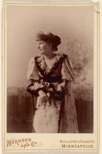[Donna non identificata di profilo, appoggiata a una sedia, con in mano un ventaglio di piume]. da Murdock and Company