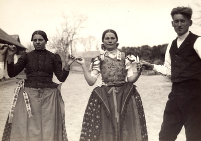 Due donne e un uomo, in abiti tradizionali ungheresi, si tengono per mano in una danza, tenendo alcune candele in mano da Rudolf Balogh