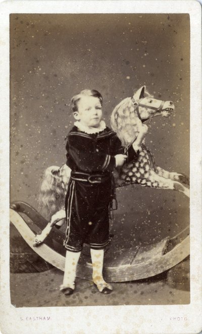 Ragazzo giovane in piedi accanto a un cavallo a dondolo da Silas Eastham