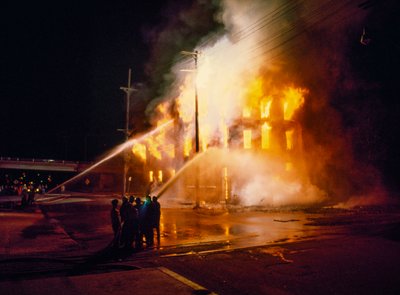 Un edificio urbano completamente avvolto dalle fiamme di notte a Kansas City con pompieri da Ted Spiegel