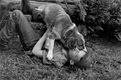 Giovane uomo gioca con il suo cane fuori dalla loro capanna di tronchi a Palmer, Alaska da Ted Spiegel