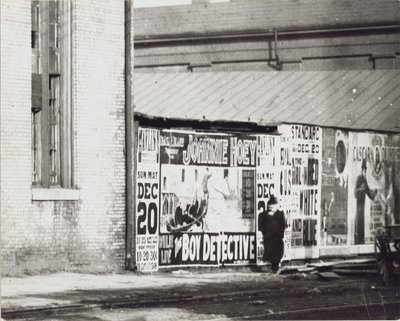 Un uomo passa davanti a un muro di manifesti pubblicitari, incluso uno per Johnnie Hoey The Boy Detective al Havlin