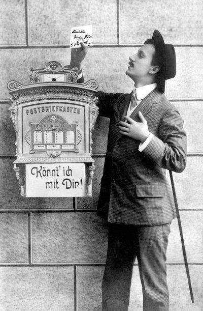 Un uomo elegante in abito, cappello e bastone, imbuca una nota in una cassetta postale. Germania intorno al 1920 da Unbekannt