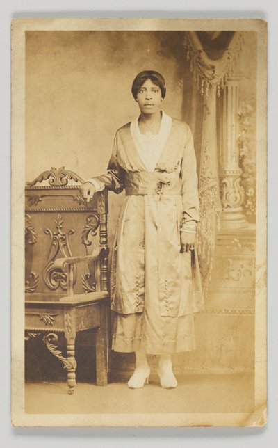 Cartolina fotografica di una donna accanto a una sedia di legno, 1904-1918 da Unbekannt
