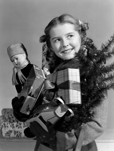 Ragazza giovane che porta un braccio pieno di regali di Natale, c 1950 da Unbekannt