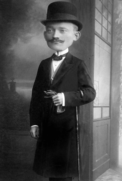 Ritratto di un uomo molto elegante con una testa gigante, indossa un cappello a melone, un bastone, un papillon e un cappotto nero. Questo è un fotomontaggio. Anni 1910 Fotografia storica, uomo con testa gigante da Unbekannter Künstler