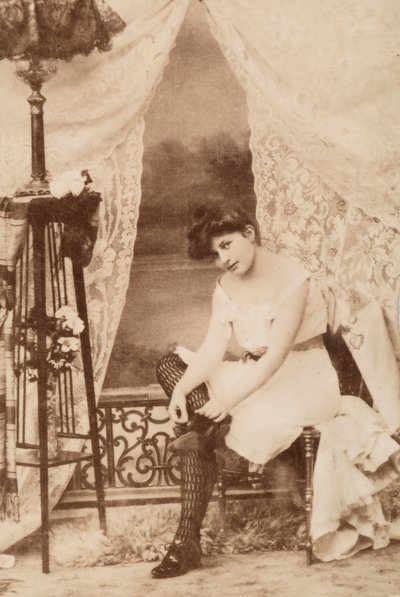 Ritratto di una giovane donna in abbigliamento intimo, seduta mentre allaccia la scarpa da Unknown photographer