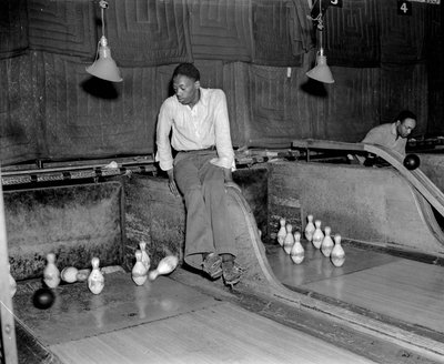 Uomo afroamericano che partecipa ai birilli in una pista da bowling, per ripristinare manualmente i birilli da Volkmar Wentzel