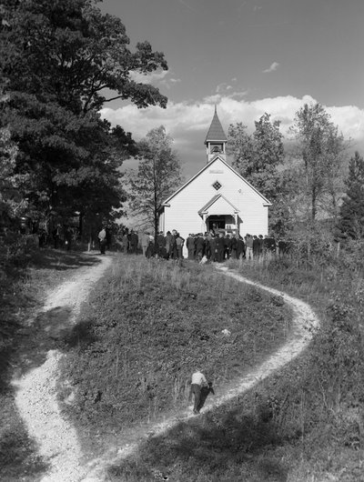 Uomini riuniti fuori da un piccolo edificio rurale, una scuola o una chiesa con campanile da Volkmar Wentzel
