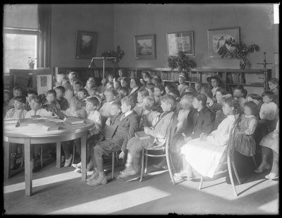 Bambini seduti, che ascoltano nella sala di lettura di una filiale non identificata della Biblioteca Pubblica del Queens Borough, c.1910 da William Davis Hassler