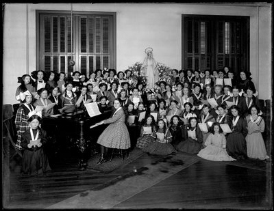 Ritratto di gruppo di una classe di coro femminile intorno a un pianoforte con spartiti, probabilmente presso l