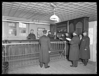 Interno di una stazione di polizia non identificata, con agenti e banco di accoglienza, c.1913-14 da William Davis Hassler
