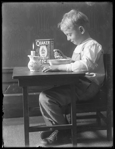 William Gray Hassler seduto a un piccolo tavolo mangiando una ciotola di cereali Quaker puffed rice, c.1912 da William Davis Hassler