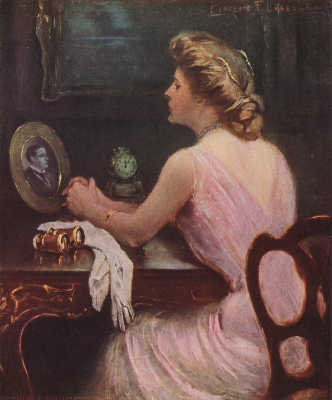 Donna seduta al suo tavolo da toeletta che guarda una fotografia di un uomo, forse suo marito o amante da Clarence F. Underwood