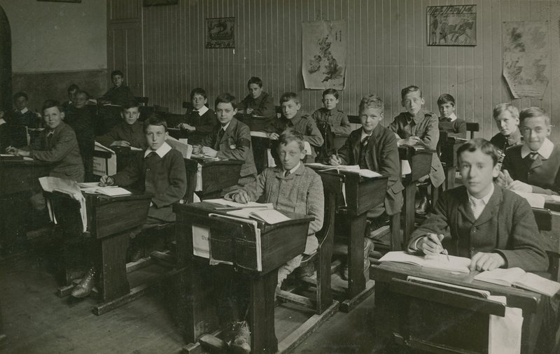Alunni maschi seduti dietro i loro banchi durante una lezione a scuola da English Photographer