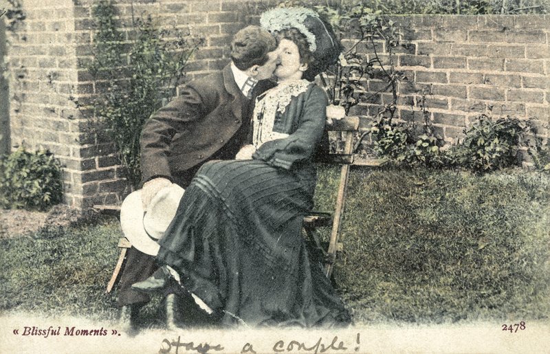 Uomo che ruba un bacio a una ragazza su una panchina da giardino da English Photographer