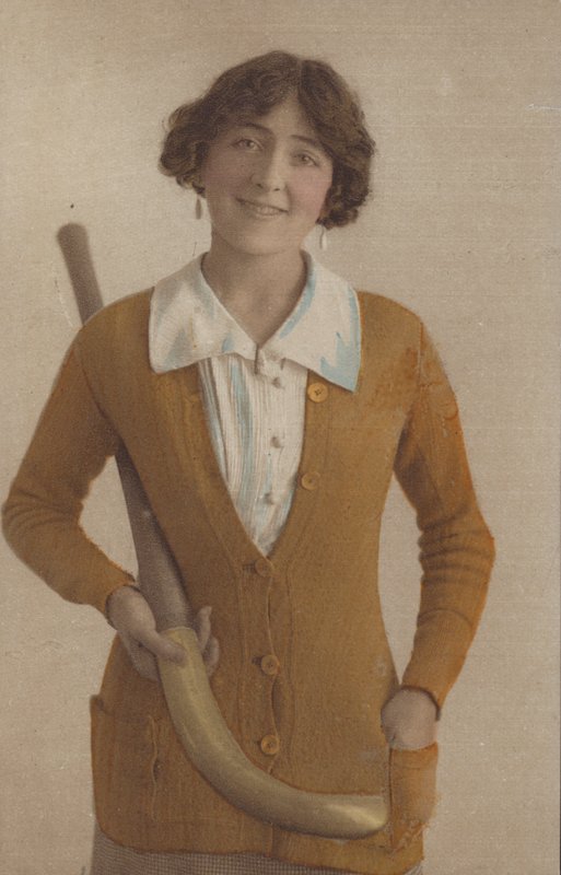 Ragazza carina, con maglione lavorato a maglia, con orecchini di perle, che tiene una mazza da hockey (foto) da English Photographer