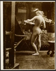 [Modella nuda in piedi in uno studio con in mano un album di schizzi].