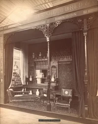 Esposizione di James Shoolbred & Co. -- Scena del salotto nel Main Building composta da una credenza e uno specchio con vasi sopra e davanti, sedie, un tavolo e un divano. Sul pavimento c