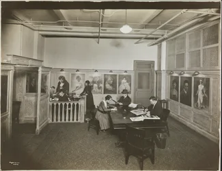 Ufficio principale/sala di ricevimento alla Mutual Film Co. con segretaria alla scrivania, persone a un tavolo che leggono e ritratti sul muro, New York